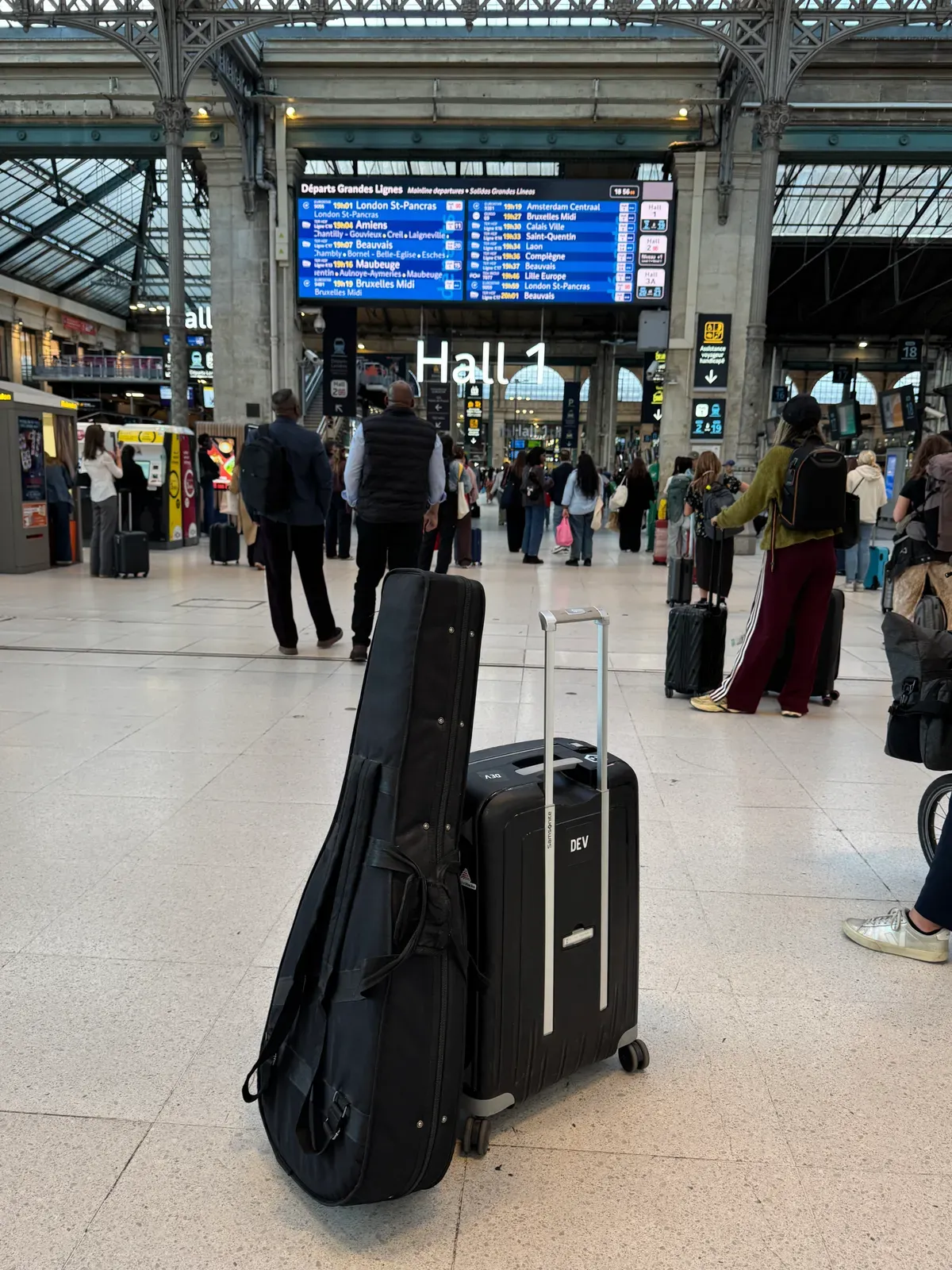 Housse de guitare et valise sous le tableau des départs dans une gare