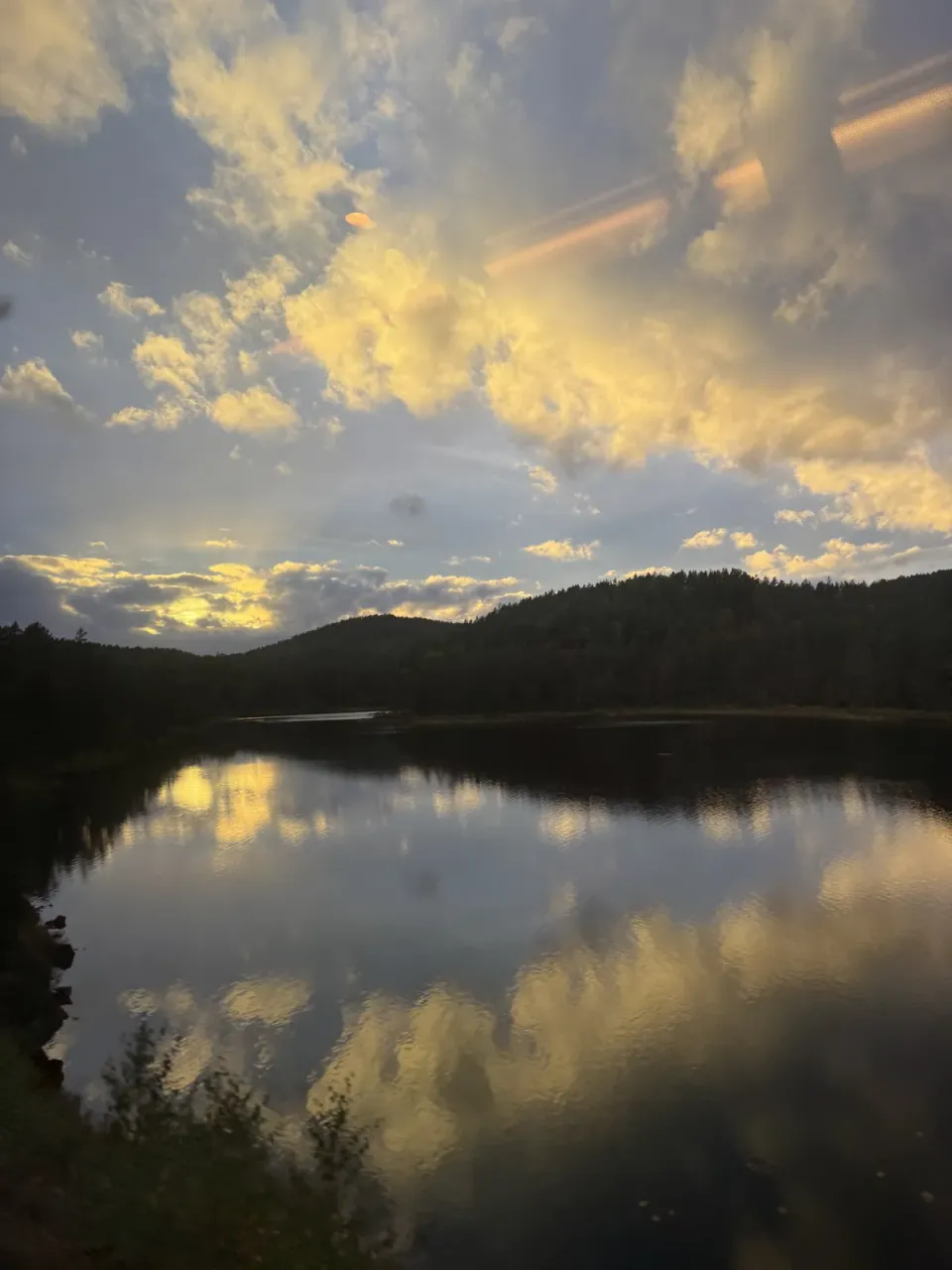 Nuages dorés et collines norvégiennes qui se reflètent dans un lac, vus du train